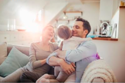 A happy family in their bright home. A young child hugs her smiling father, while the mother looks on, conveying comfort and peace.