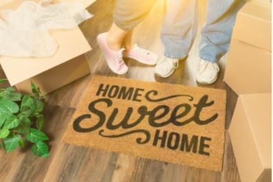 Two peoples feet behind a floor mat that says home sweet home.